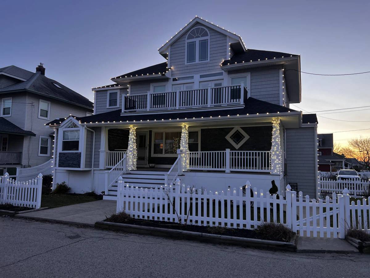 Holiday garland and warm white lights on a coastal-style front porch