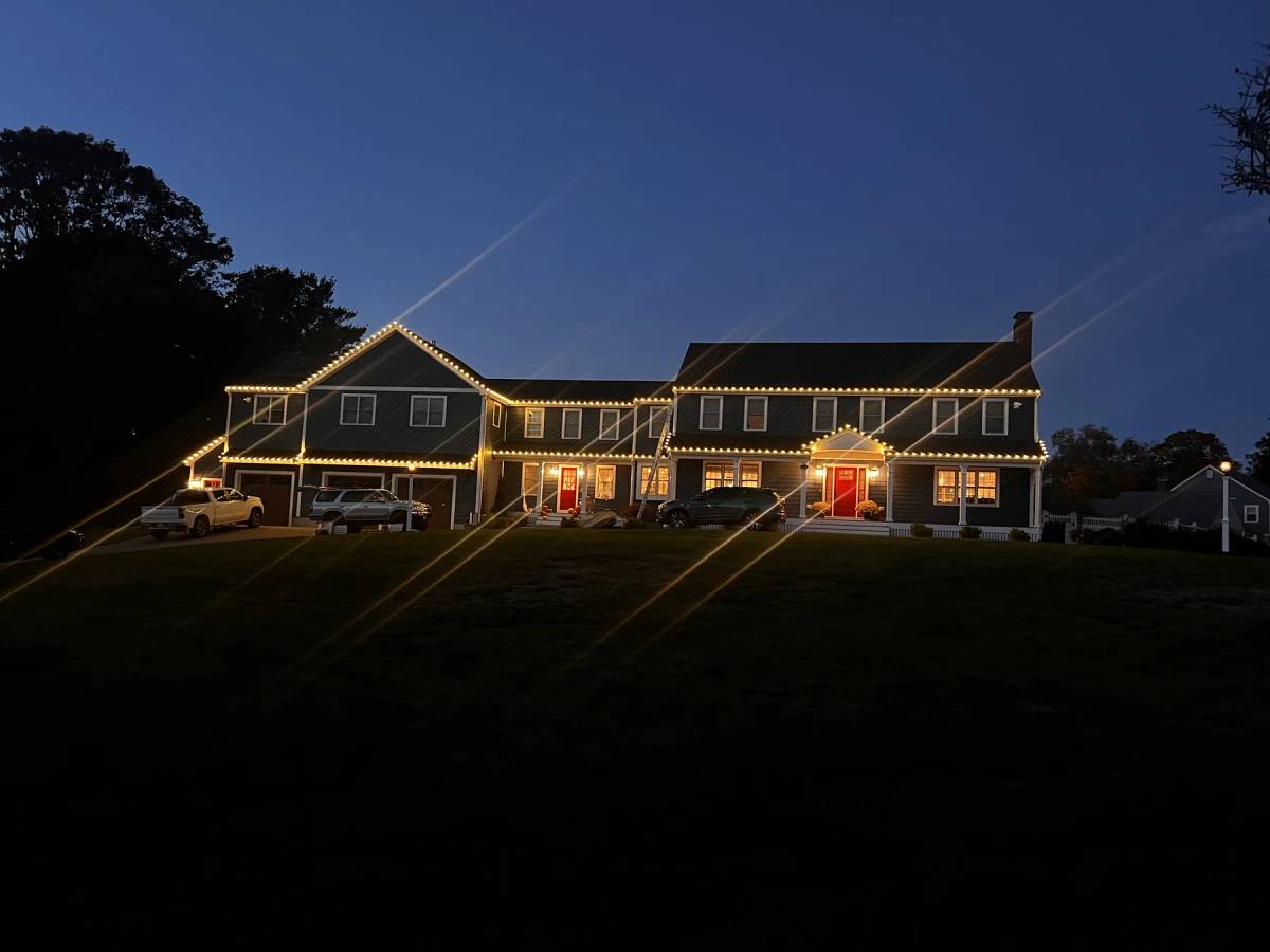 Warm holiday roofline lights on a wide home at dusk